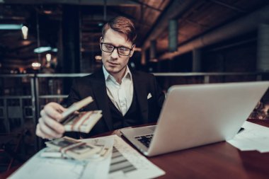 Dizüstü bilgisayar kullanarak bir iş adamı. Genç iş adamı. Giyim siyah takım elbiseli biri. Deneyimli girişimci. Tablo sıkı adam Laptop. Geç saatlere kadar. Holding ve sayımın para. paraya bak