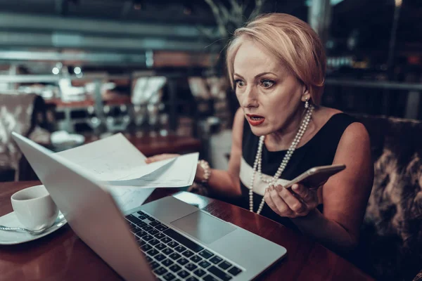 Businesswoman Using Laptop. Old Businesswoman looking Laptop . Experienced Entrepreneur. Working Late. Success Grandmother. Sits in Office. holds paper with Graphics. surprised woman.