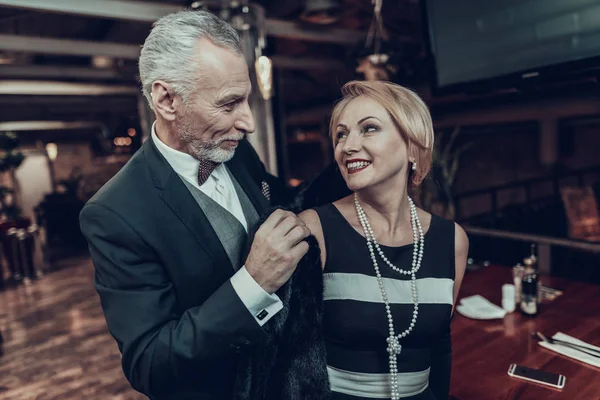 Businesswoman and Businessman . Old Business People .Successful Old People. Relax together. Romantic Meeting, Rich People. Couple Resting in Restaurant. helps woman get dressed. caring for lady