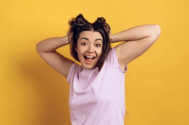 Genç kız neşeli teline uzun katlar. Sarı arka plan üzerinde izole. Stüdyo portre.