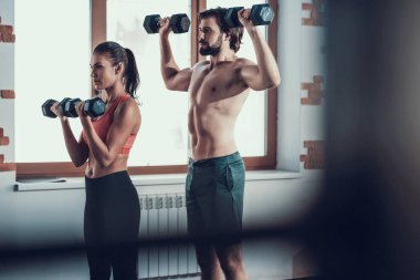 Kız ve adam salonunda Dumbbells egzersizleri yapıyor. Training Day. Fitness Kulübü. Sağlıklı bir yaşam tarzı. Güçlü sporcular. Aktif tatiller. CrossFit kavramı. Sporcu T gömlek olmadan. Güneşli gün.