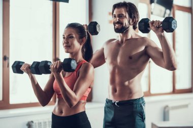 Kız ve adam salonunda Dumbbells egzersizleri yapıyor. Training Day. Fitness Kulübü. Sağlıklı bir yaşam tarzı. Güçlü sporcular. Aktif tatiller. CrossFit kavramı. Sporcu T gömlek olmadan. Güneşli gün.