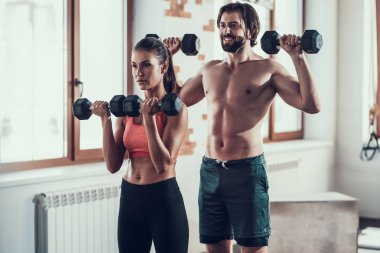 Kız ve adam salonunda Dumbbells egzersizleri yapıyor. Training Day. Fitness Kulübü. Sağlıklı bir yaşam tarzı. Güçlü sporcular. Aktif tatiller. CrossFit kavramı. Sporcu T gömlek olmadan. Güneşli gün.