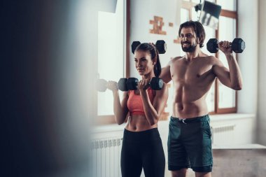 Kız ve adam salonunda Dumbbells egzersizleri yapıyor. Training Day. Fitness Kulübü. Sağlıklı bir yaşam tarzı. Güçlü sporcular. Aktif tatiller. CrossFit kavramı. Sporcu T gömlek olmadan. Güneşli gün.
