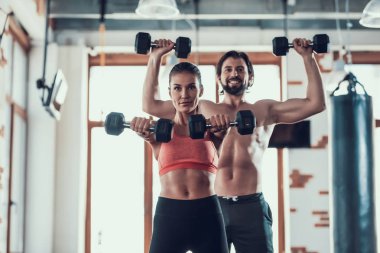 Kız ve adam salonunda Dumbbells egzersizleri yapıyor. Training Day. Fitness Kulübü. Sağlıklı bir yaşam tarzı. Güçlü sporcular. Aktif tatiller. CrossFit kavramı. Sporcu T gömlek olmadan. Güneşli gün.