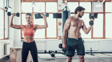 Kız ve adam salonunda Dumbbells egzersizleri yapıyor. Training Day. Fitness Kulübü. Sağlıklı bir yaşam tarzı. Güçlü sporcular. Aktif tatiller. CrossFit kavramı. Sporcu T gömlek olmadan. Güneşli gün.