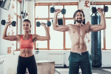 Kız ve adam salonunda Dumbbells egzersizleri yapıyor. Training Day. Fitness Kulübü. Sağlıklı bir yaşam tarzı. Güçlü sporcular. Aktif tatiller. CrossFit kavramı. Sporcu T gömlek olmadan. Güneşli gün.