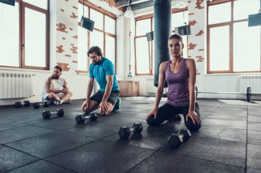 İki adam ve kız spor salonu zemin üzerinde bekletin. Mola zamanı. Training Day. Fitness Kulübü. Sağlıklı bir yaşam tarzı. Aktif tatiller. CrossFit kavramı. Yorgun sporcular. Dambıl ile otur. Tükenmiş sporcular.