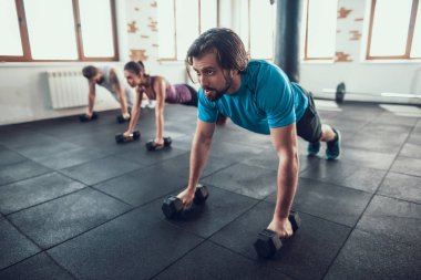 İki adam ve kadın iş Dumbbells üzerinde Ups itin. Training Day. Fitness Kulübü. Sağlıklı bir yaşam tarzı. Güçlü atlet. Aktif tatiller. CrossFit kavramı. Parlak spor salonu. Rahat spor giyim.