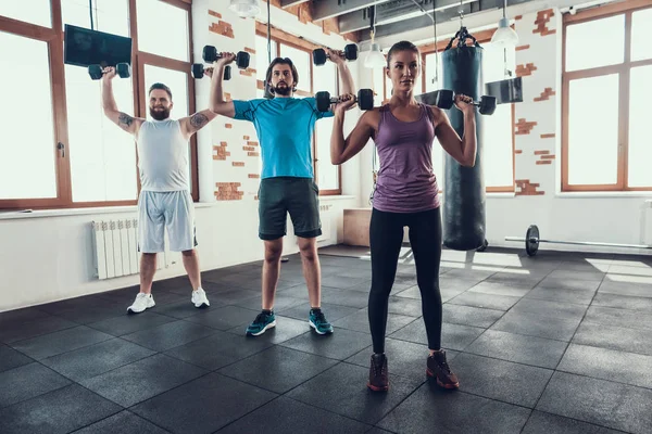 女孩和两个男人举起哑铃 培训日 健身俱乐部 健康的生活方式 强大的运动员 活动假期 交叉的概念 明亮的健身房 舒适的运动装 坚强的人 — 图库照片