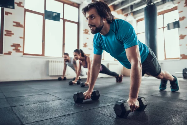 两个男人和女人在哑铃上推 Ups 培训日 健身俱乐部 健康的生活方式 强大的运动员 活动假期 交叉的概念 明亮的健身房 舒适的运动装 — 图库照片