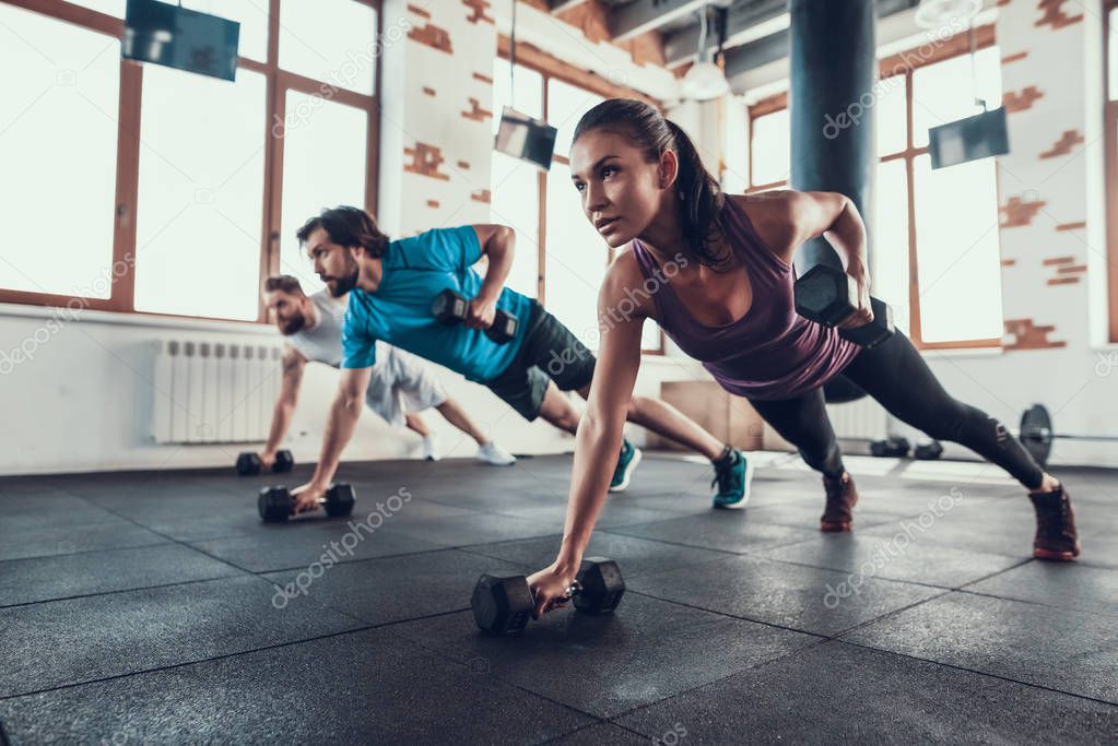 Athletes On The Floor. Dumbbell Lift With One Hand. Training Day. Fitness Club. Healthy Lifestyle. Powerful Athlete. Active Holidays. Crossfit Concept. Bright Gym. Comfortable Sportswear.