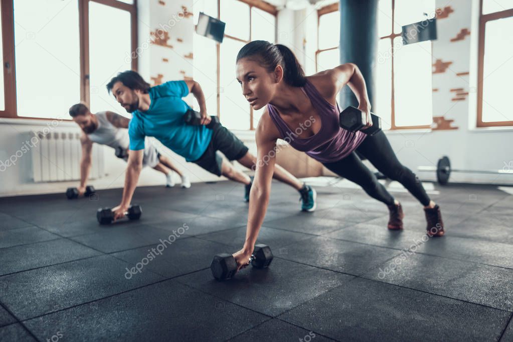 Athletes On The Floor. Dumbbell Lift With One Hand. Training Day. Fitness Club. Healthy Lifestyle. Powerful Athlete. Active Holidays. Crossfit Concept. Bright Gym. Comfortable Sportswear.