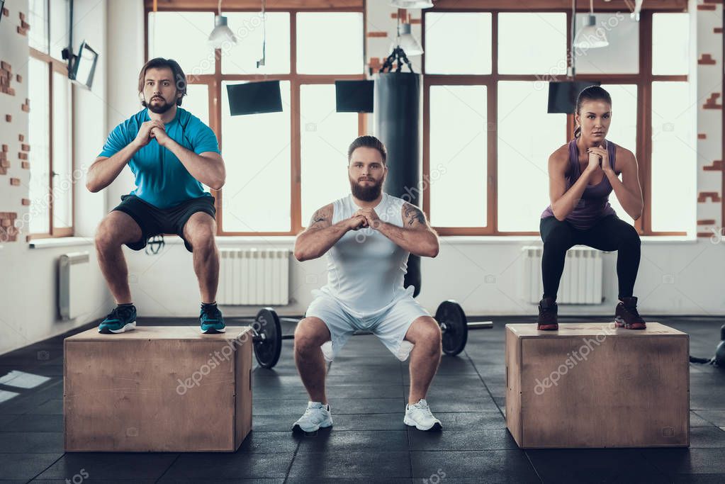 Two Men And Woman Doing Squats Exercises. Training Day. Fitness Club. Healthy Lifestyle. Powerful Athlete. Active Holidays. Crossfit Concept. Spacious Bright Gym. Comfortable Sportswear.