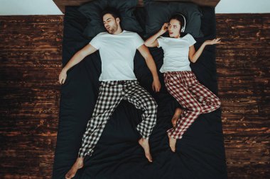 Çift yatakta Lying olduğunu. Çift genç güzel kadın ve erkek adam uyku ve Snores. Dissatisfied ve kulaklık ile onun kulakları kapsayan bir kadındır. İnsanlar ev iç. Üstten görünüm.