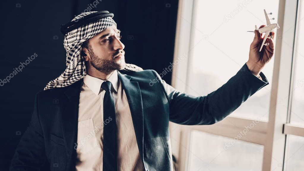 Arab Businessman. Man Wearing in Black Suit. Experienced Entrepreneur. Successful Young Man. standing near window . green Office. Portrait of Arab. played by an airplane model. cropped photo