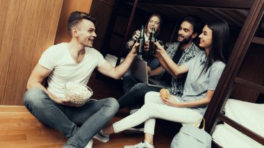 Hostel genç insanlar için. Seyahat arkadaşlarım. Hostel küçük odada. Birlikte vakit. gülümseyen kadın. Yatağın üstüne oturan arkadaşlar. birlikte sakin ol. yemek ve içki. Şerefe. patlamış mısır tutar