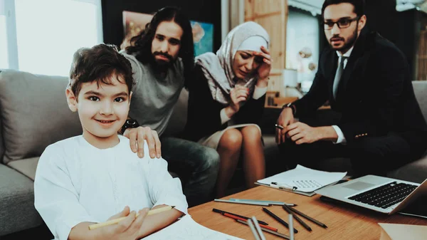 Arab Family at Reception in Psychotherapist. Family is Father, Mother and Son. Psychotherapist is Caucasian Man. Boy is Smiles. Doctor and Father is Looking on Boy. Mother is Sad and Crying.