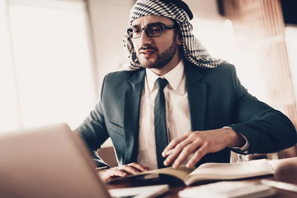 アラブのビジネスマン 黒のスーツを着ている男 経験豊富な起業家 オフィスで仕事を成功した若い男 アラビア人の肖像画メガネでアラブ ノートに書き込みます テーブルの近くの男 ノート パソコンをお探し — ストック写真