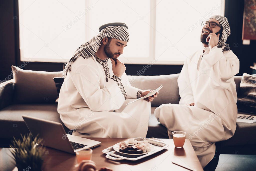 Arabs Businessman. Men Wearing in white clothes. Experienced Entrepreneur. Successful Young Men. Portrait of Arab. Work in Office. Arab hold paper. talking on phone. conversation. Laptop on table