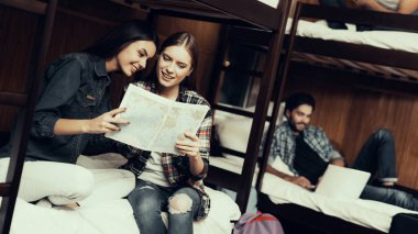 Hostel genç insanlar için. Seyahat arkadaşlarım. Hostel küçük odada. Birlikte vakit. ranza yatak odasında. Yatağa otur. gülümseyen kız. En iyi dostlar. Erkekler bekletin. Haritaya bak. harita tutmak.