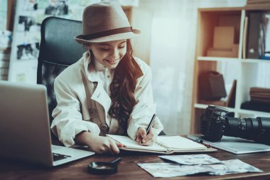 Dedektif Özel Dedektiflik Bürosu 'nda çalışıyor. Dedektif Kafkasyalı Küçük Kız. Not Defterine Not Yazan Kız. Masa 'da oturan kişi. Kız Pelerin ve Şapka Giyiyor. Çocuk gülümsüyor..