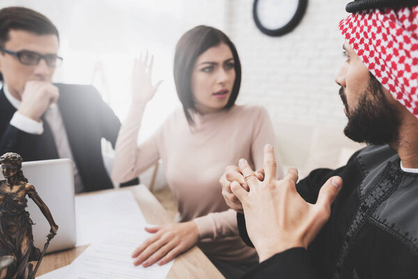 Lawyer in suit in office with arab husband and wife. Man is removing wedding ring from his finger.