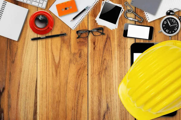 Top view desk engineer with yellow helmet, smart phone, coffee cup, paper note, glasses and office equipment.