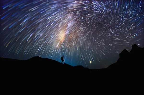 Silhouette of man with backpack on hill watching the stars at night, long exposure.