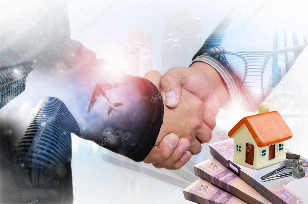 Handshake  with real estate agents, house models on banknotes and keys. The concept of home trading agreement.