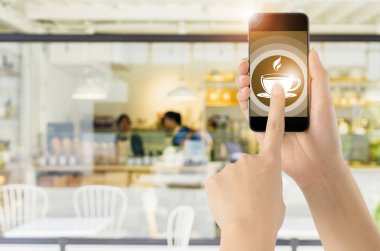 Dokunmatik ekran akıllı telefon kahve simgesini bulanık kahve dükkanı arka plan ile. Kavram Gıda online.