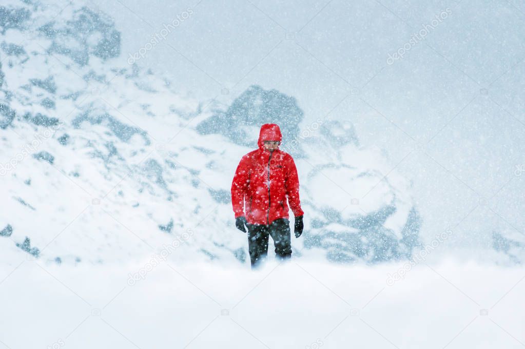 Man with red overcoat walking on a snow covered path during a snowfall.
