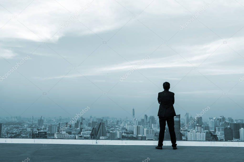Businessman standing on top of building and viewing modern city.