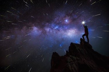 Dağcı veya backpacker silüeti. Elinde, o başını yüksek ışık düzenlenen. Kayalık dağ tepe ve Samanyolu Gökadası, başarı, kazanan, lider kavramı üzerinde duruyor. Yüksek ISO gürültü ile.