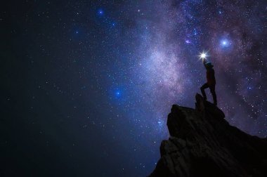 Dağcı veya backpacker silüeti. Elinde, o başını yüksek ışık düzenlenen. Kayalık dağ tepe ve Samanyolu Gökadası, başarı, kazanan, lider kavramı üzerinde duruyor. Yüksek ISO gürültü ile.