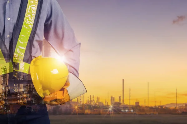 ぼやけて石油製油所背景 労働者の安全のための黄色いヘルメットを保持しているエンジニアの二重露光 — ストック写真