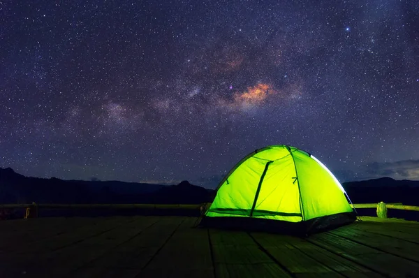 Glowing green camping tent on bamboo terrace under the night sky full of stars and the Milky Way, Baan Jabo, Mae Hong Son, Thailand. leisure tourists.