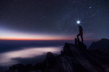Dağcı veya backpacker silüeti. Elinde, o başını yüksek ışık düzenlenen. Kayalık dağ tepe ve Samanyolu Gökadası, başarı, kazanan, lider kavramı üzerinde duruyor. Yüksek ISO gürültü ile.