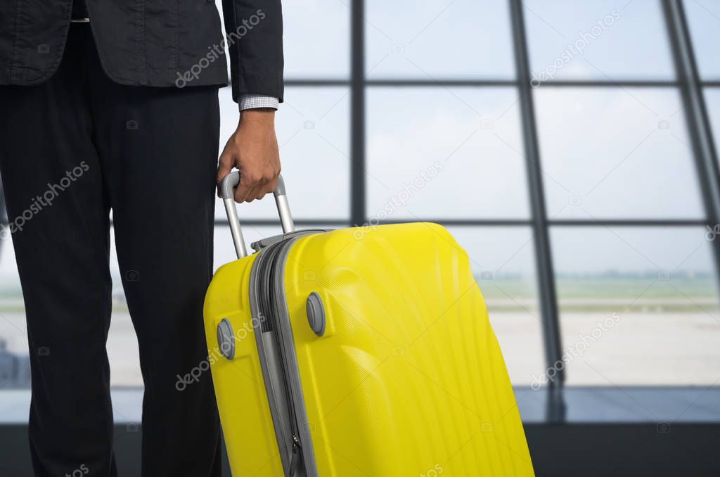 Businessman and suitcase in the airport at departure lounge, airplane in the blurred background, summer vacation concept, traveler suitcases in airport terminal waiting area 