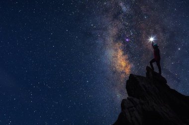 Dağcı veya backpacker silüeti. Elinde, o başını yüksek ışık düzenlenen. Kayalık dağ tepe ve Samanyolu Gökadası, başarı, kazanan, lider kavramı üzerinde duruyor. Yüksek ISO gürültü ile.