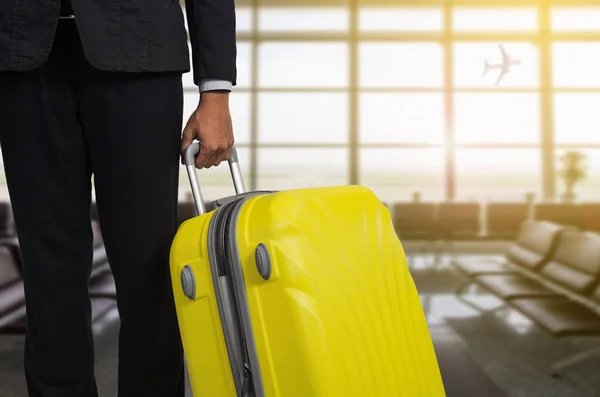 Businessman and suitcase in the airport at departure lounge, airplane in the blurred background, summer vacation concept, traveler suitcases in airport terminal waiting area