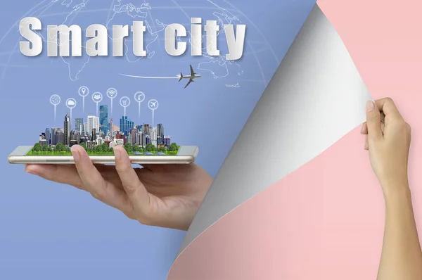 Smart city, Woman hand turning blank paper page to new page with modern building and icon internet of things (IOT), airplane, world map on smart phone in hand, Communication wireless network.