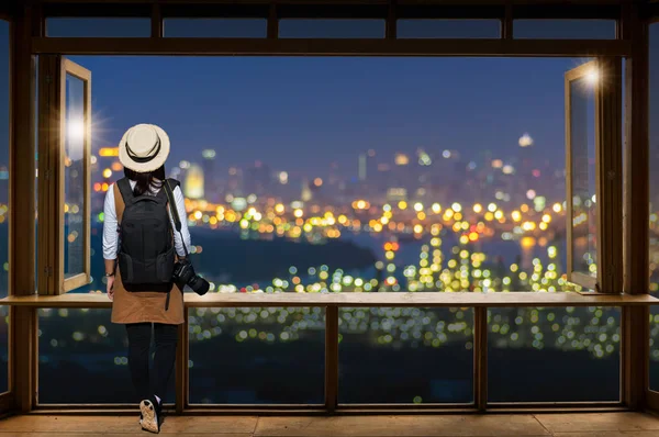 Asian female tourist wears casual clothing with simple backpack and camera looking at bangkok city view.