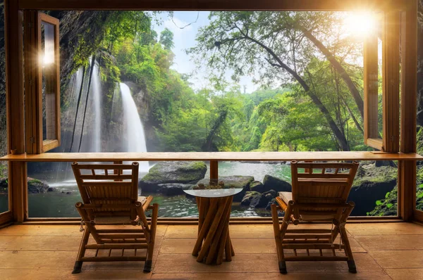 Beautiful landscape at cafe in minimal style with wooden tables and chairs on terrace against the outdoor waterfall view in cafe at sunrise.