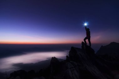 Dağcı veya backpacker silüeti. Kayalık dağ tepe ve gündoğumu, başarı, kazanan, lider kavramı üzerinde duran. 