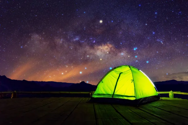 Glowing green camping tent on bamboo terrace under the night sky full of stars and the Milky Way, Baan Jabo, Mae Hong Son, Thailand. leisure tourists.