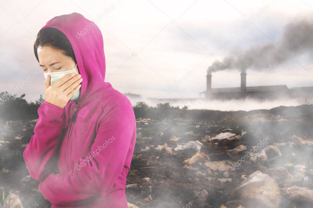 Woman sneezing, woman dressed in pink winter clothing wearing mask on face against air pollution background