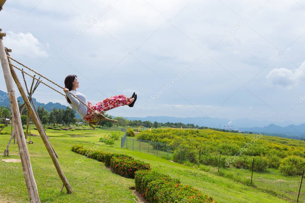 Woman wearing red dress sitting on swing on clear day in Tung Bua Tong Mexican sunflower field in Mae Moh Coal Mine, Lampang Province, Thailand.