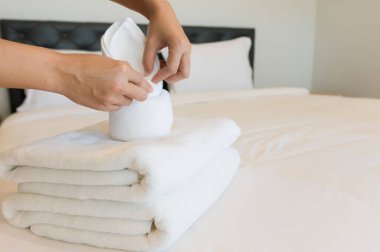 Bir otel odasında yumuşak havlu koyarak genç otel hizmetçisi. havlu temiz beyaz bir battaniye ile bir yastık yatak odasında yatağın üstüne yerleştirilir sabah.