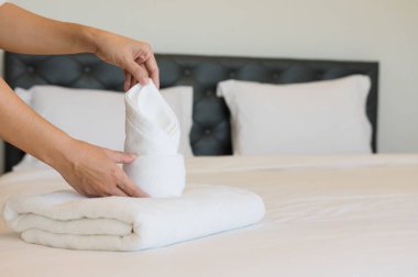 Bir otel odasında yumuşak havlu koyarak genç otel hizmetçisi. havlu temiz beyaz bir battaniye ile bir yastık yatak odasında yatağın üstüne yerleştirilir sabah.